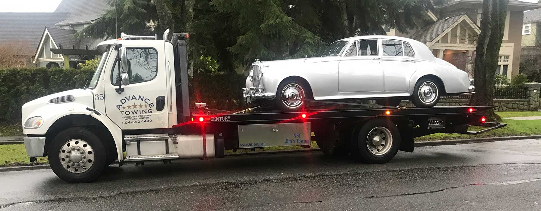 A Luxury Vehicle towed by a advance towing truck on a city street
