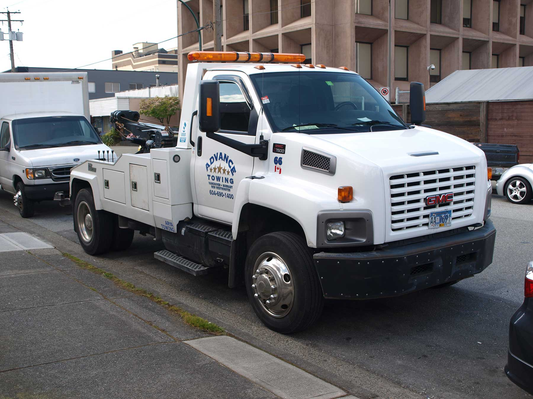 A white tow truck parked on the side of the road offers Advance Towing long haul car towing services