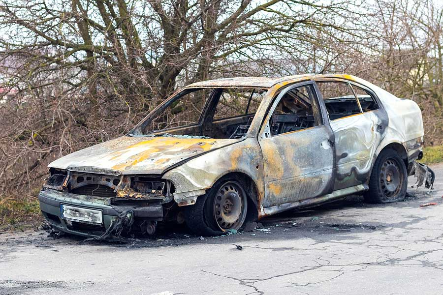 a burnt out car sitting on the side of a road